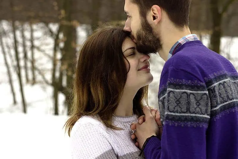 Ein Mann draußen im Schnee küsst eine Frau auf die Stirn