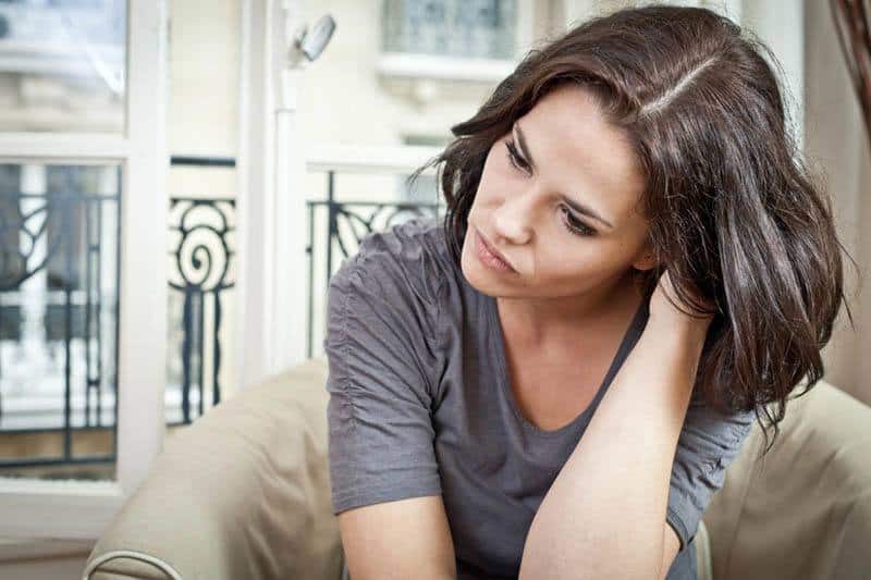 Brünette Frau, die zu Hause sitzt, sieht nachdenklich aus