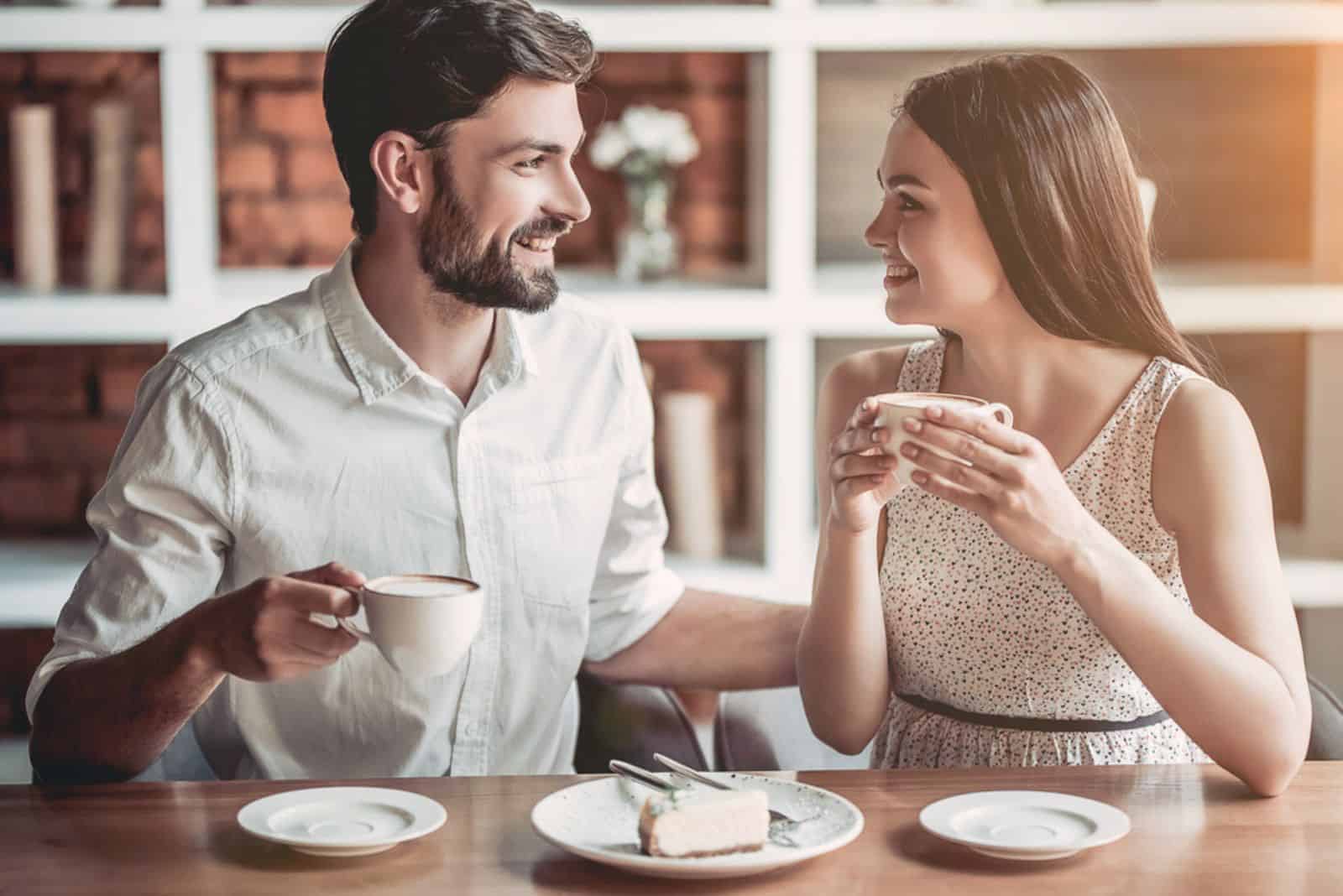 Ein schönes Mädchen mit langen braunen Haaren sitzt neben einem Mann und sie trinken Kaffee