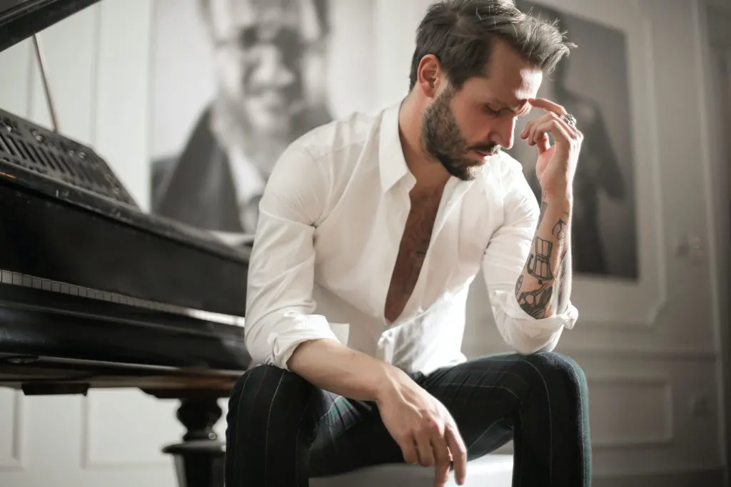 Ein trauriger Mann mit einem Tattoo auf dem Arm sitzt neben einem Klavier