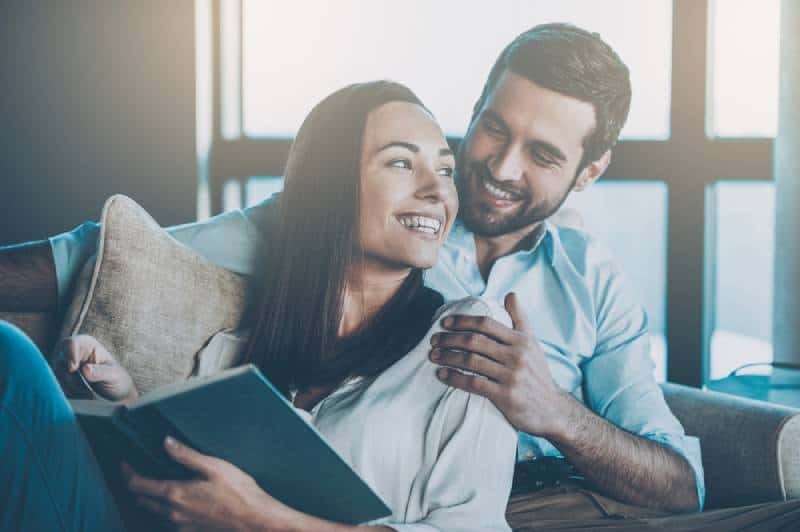 Schönes junges liebendes Paar, das aneinander bindet und lächelt, während Frau ein Buch hält