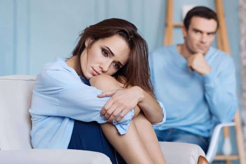 Verärgerte junge Frau, die zu Hause neben seinem Ehemann sitzt
