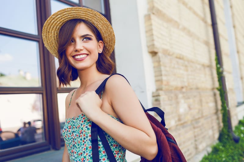 ein junges lächelndes Mädchen mit einem Hut und einem Rucksack auf dem Rücken