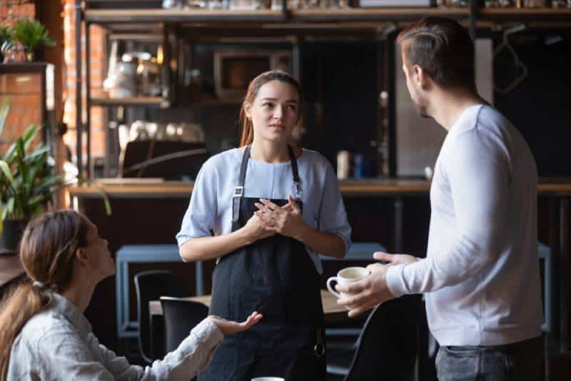 wütendes Restaurant-Kundenpaar im Gespräch mit Kellnern in der Öffentlichkeit
