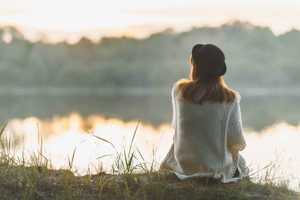 Das Mädchen mit dem Hut sitzt alleine am Flussufer