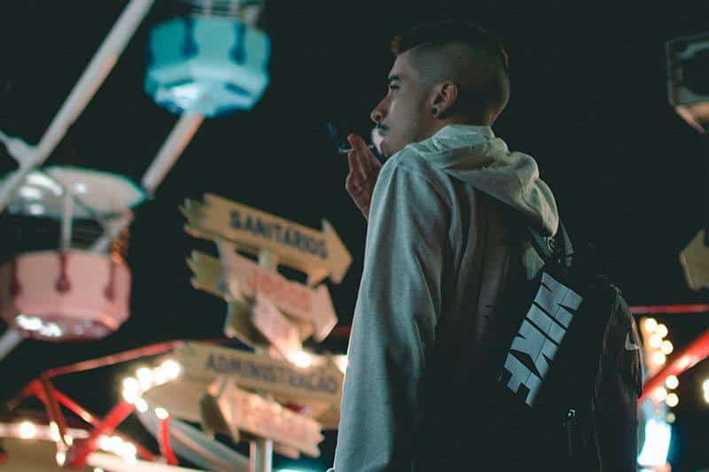 Ein Mann in einem grauen Sweatshirt mit einem Rucksack auf dem Rücken raucht eine Zigarette