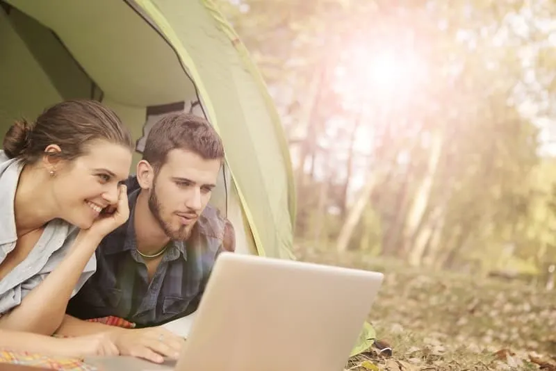 Ein Mann und eine Frau liegen in einem Zelt und beobachten etwas auf einem Laptop