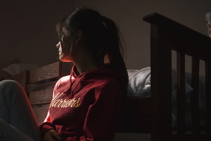 Eine traurige Frau in einem roten Sweatshirt sitzt auf dem Boden des Schlafzimmers