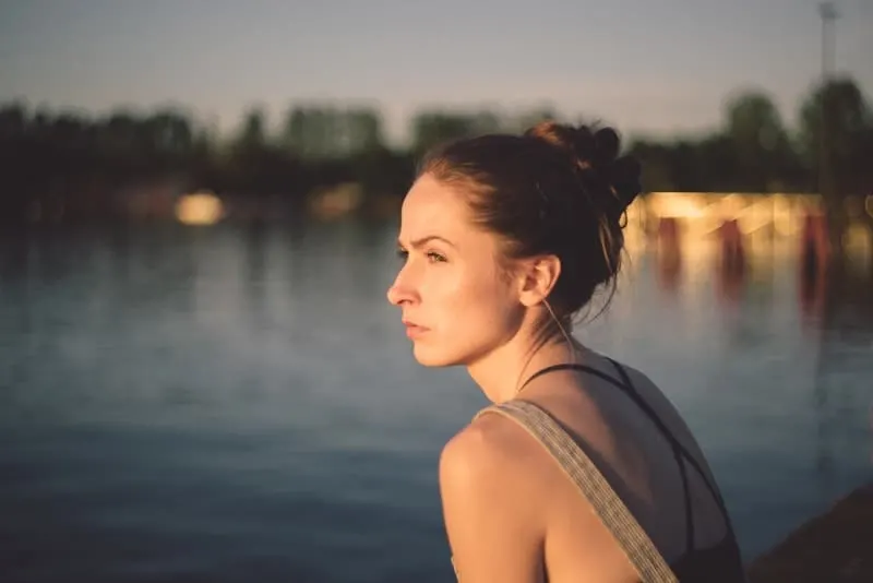 eine depressive Frau, die bei Sonnenuntergang am Wasser steht