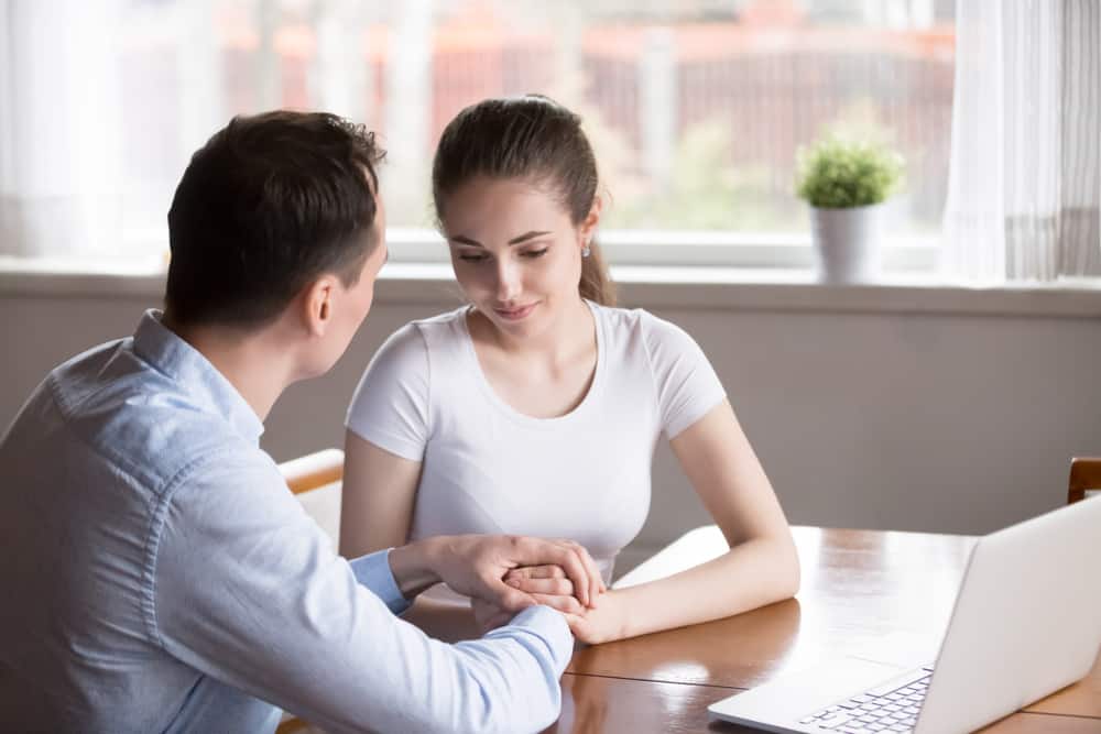 Der Mann sitzt mit seiner Frau am Tisch und hält seine Hand