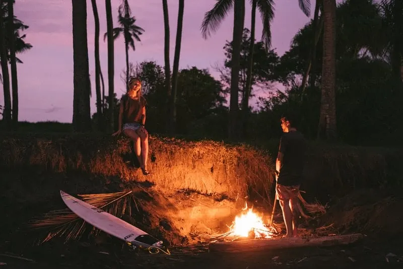 Ein Mann und eine Frau am Lagerfeuer am Strand unter Palmen