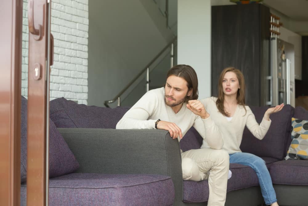 Ein frustrierter wütender Mann sitzt auf der Couch und eine Frau erzählt ihm etwas
