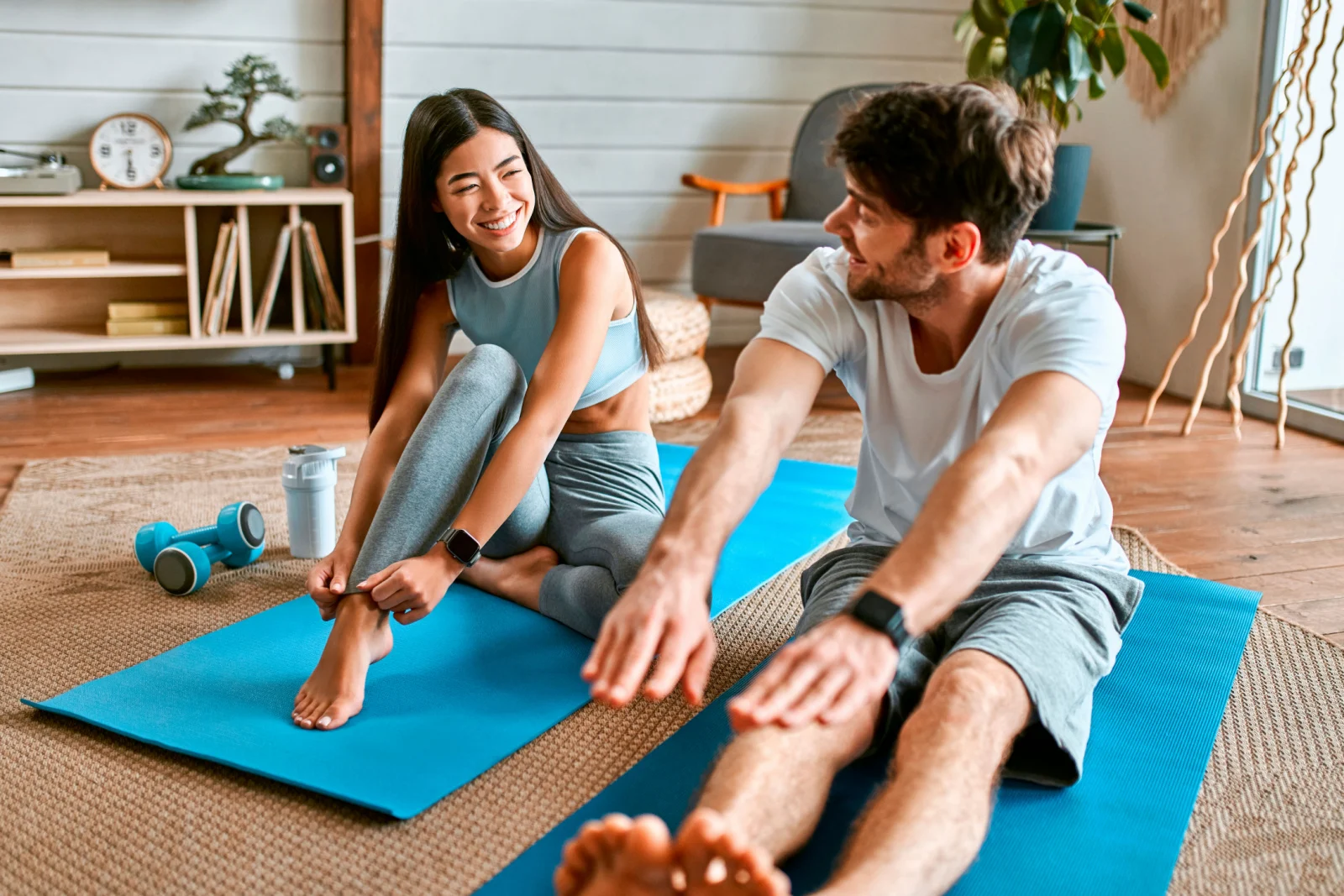 Ein junges Paar in Sportkleidung macht zu Hause in einem hellen, gemütlichen Wohnzimmer Übungen auf Matten.