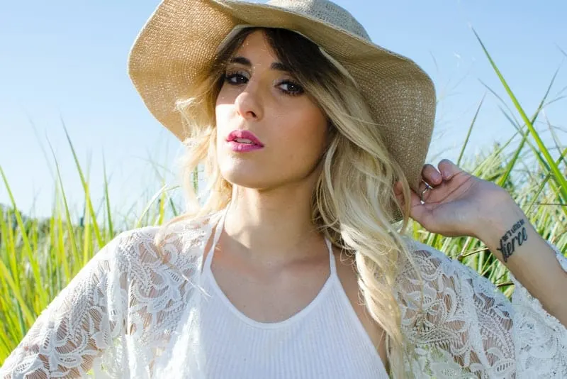 Eine Blondine mit einem Hut auf dem Kopf sitzt auf einem Grasfeld