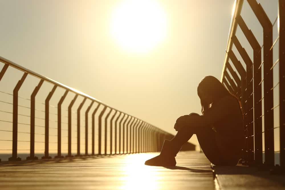 Eine depressive junge Frau sitzt mit gesenktem Kopf auf einer Brücke
