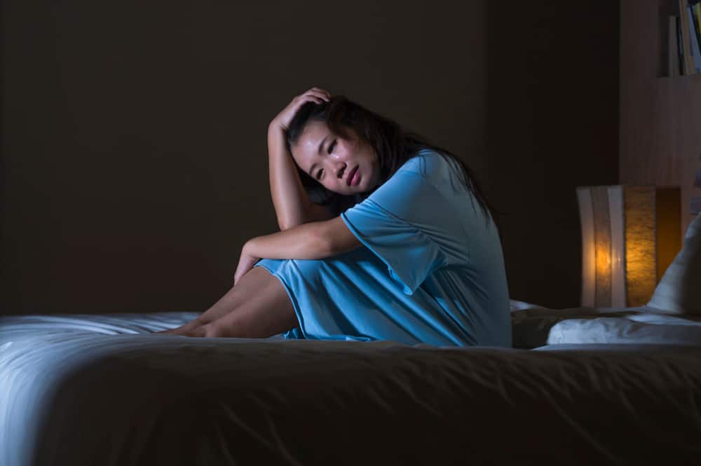 Eine traurige asiatische Frau sitzt abends auf dem Bett und weint
