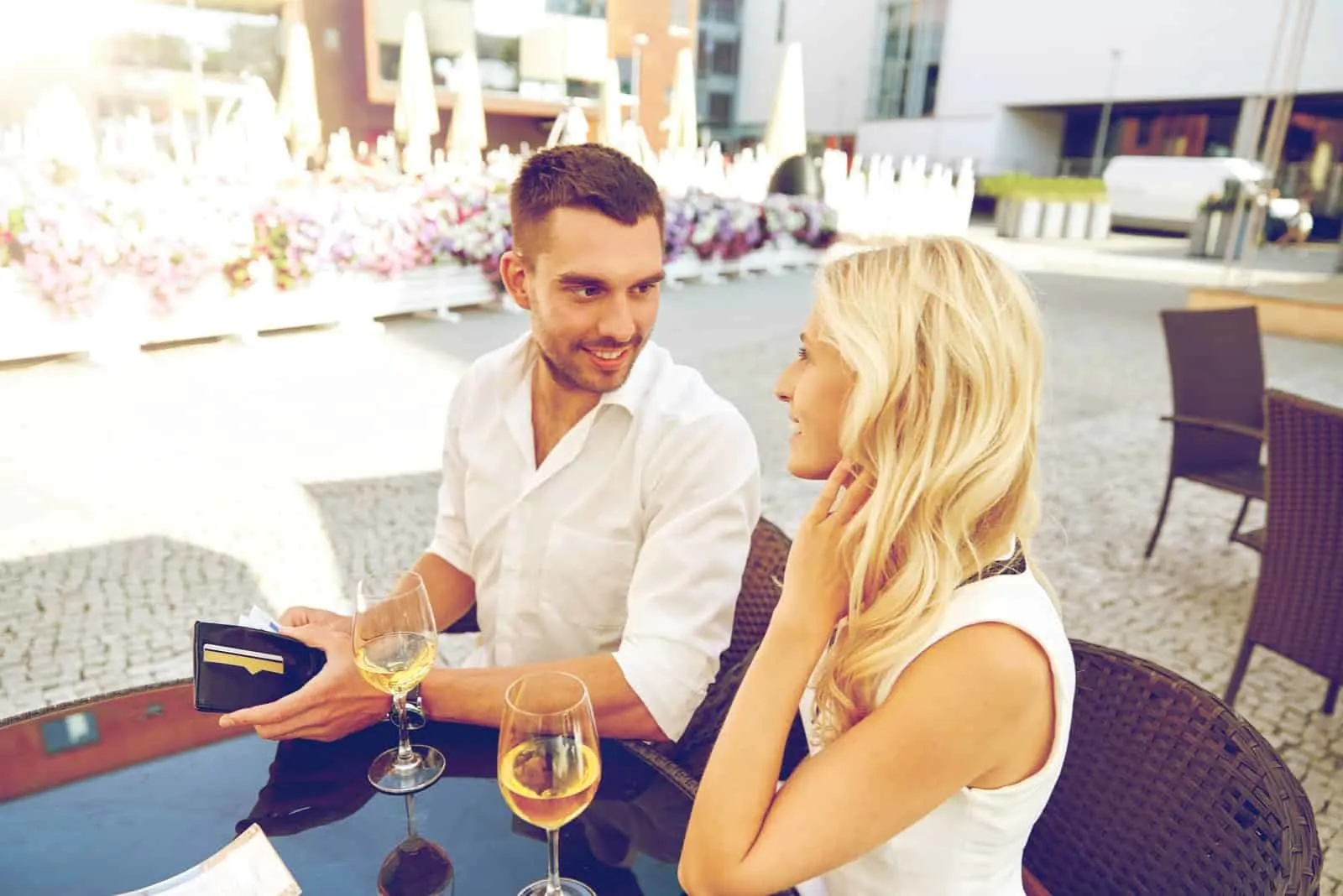 Glückliches Paar mit Brieftasche und Weingläsern, das die Rechnung im Restaurant bezahlt