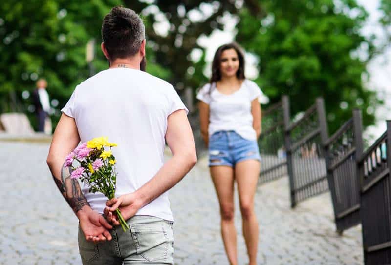 Mann hält Blumen und wartet auf Freundin