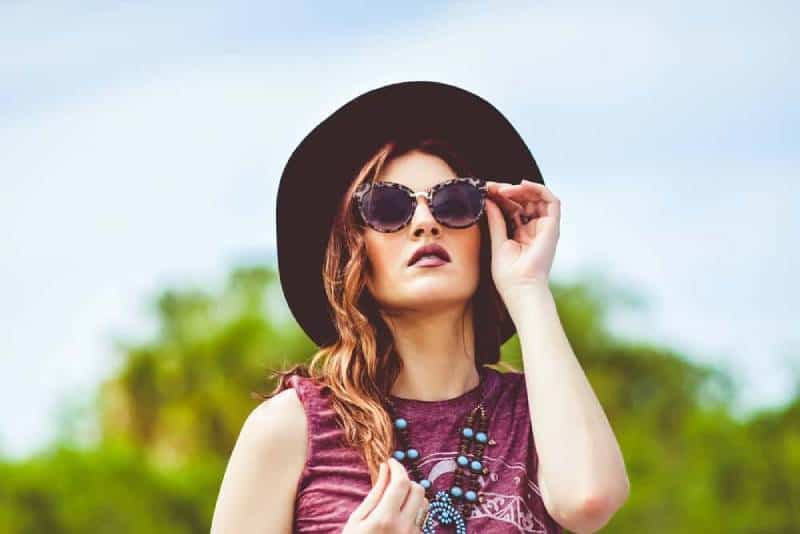 Mädchen im rosa Trägershirt, das schwarzen Sonnenhut und schwarze Sonnenbrille trägt