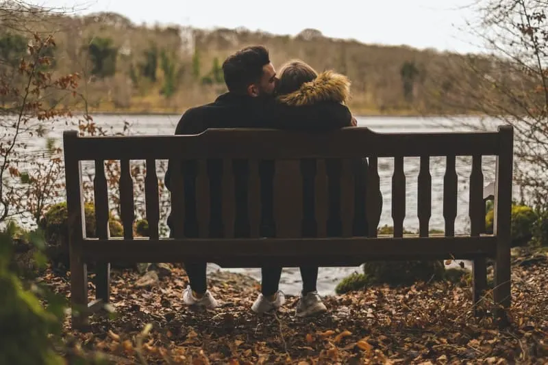 ein liebendes Paar am Ufer eines Flusses, das in einer Umarmung auf einer Bank sitzt