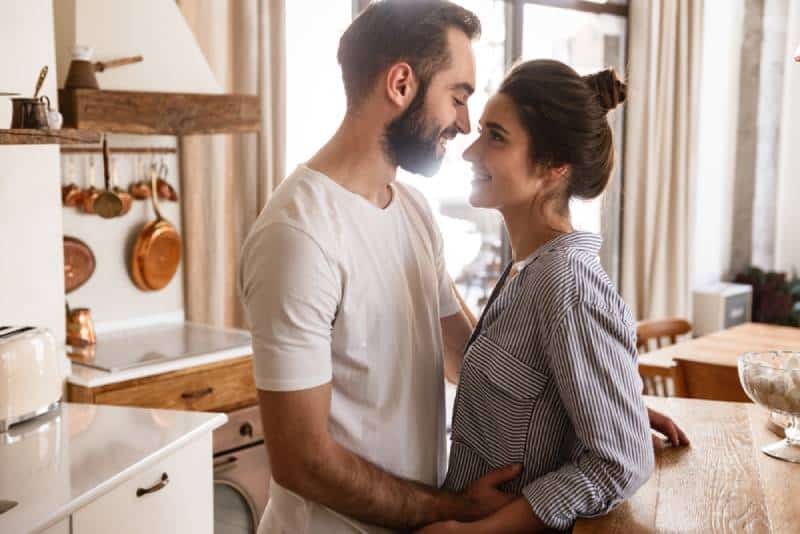 entzückendes brünettes Paar, das lächelt, während es zu Hause zusammen umarmt