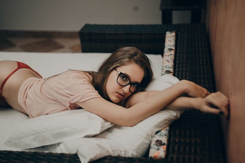 sexy Frau in Brille und Dessous auf dem Bett liegen