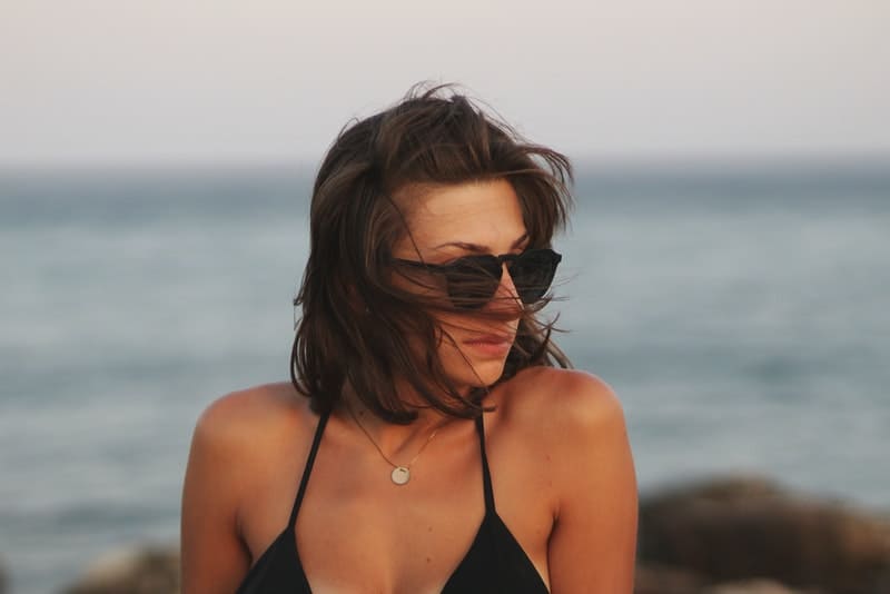 Brünette mit Sonnenbrille am Strand sitzen