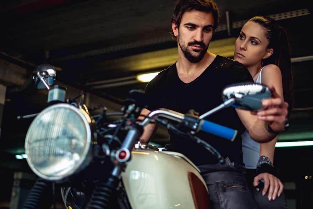 Ein Mann auf einem Motorrad sieht seine Frau im Rückspiegel an