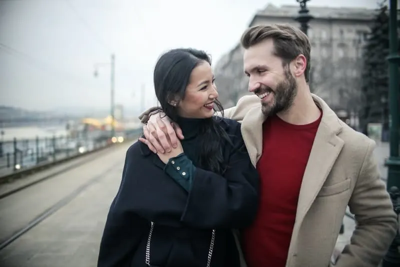 Ein Mann mit Bart und seine asiatische Frau gehen umarmend herum