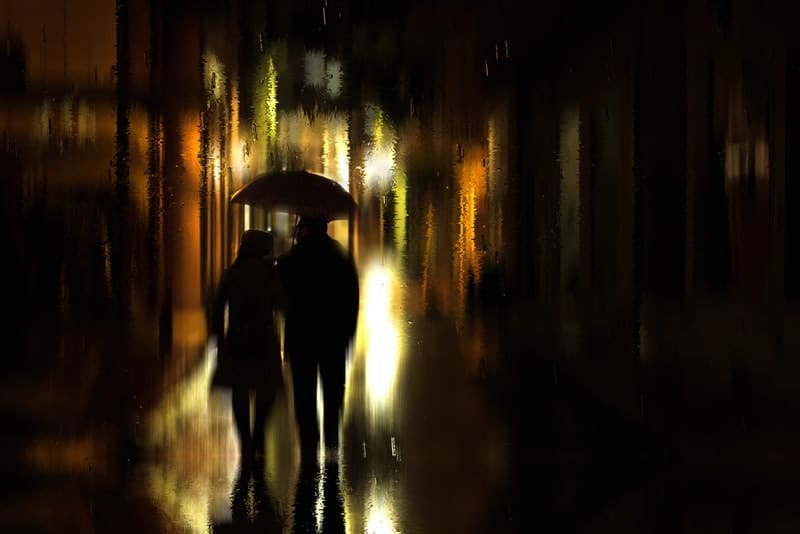 Ein Mann und eine Frau unter einem Regenschirm spazieren im Nachtregen durch die Stadt
