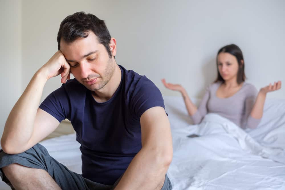 Ein besorgter Mann und eine überraschte Frau sitzen im Bett