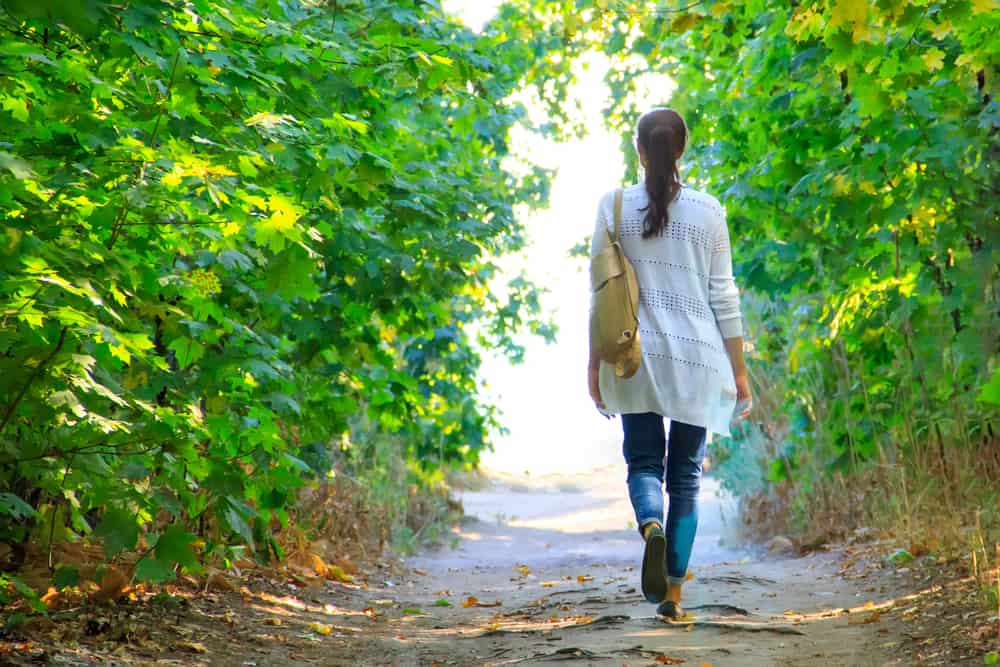 Eine Frau in einem weißen Poloshirt mit einer Geldbörse geht in der Natur spazieren
