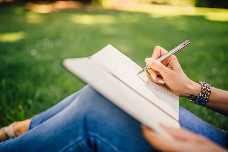 Eine Frau sitzt im Gras und schreibt etwas in ein Notizbuch