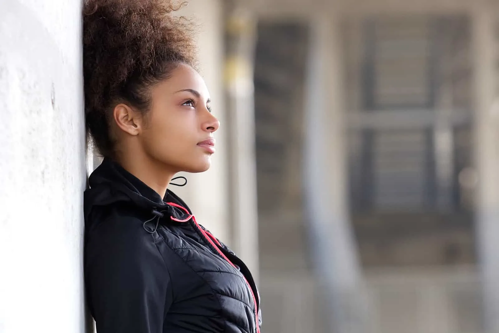 Eine junge attraktive schwarze Frau lehnt an einer Betonwand und denkt nach