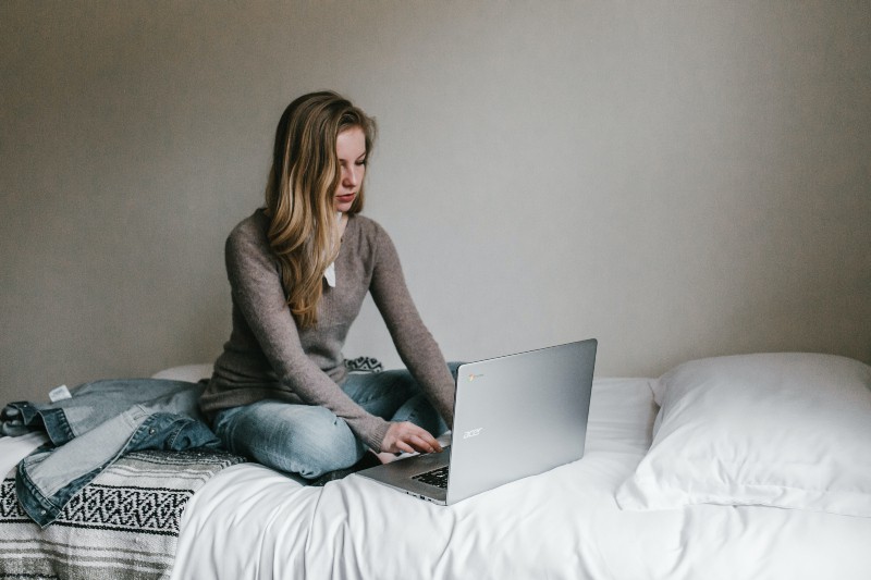 Frau, die auf MacBook Pro tippt, während sie auf Bett im Zimmer sitzt