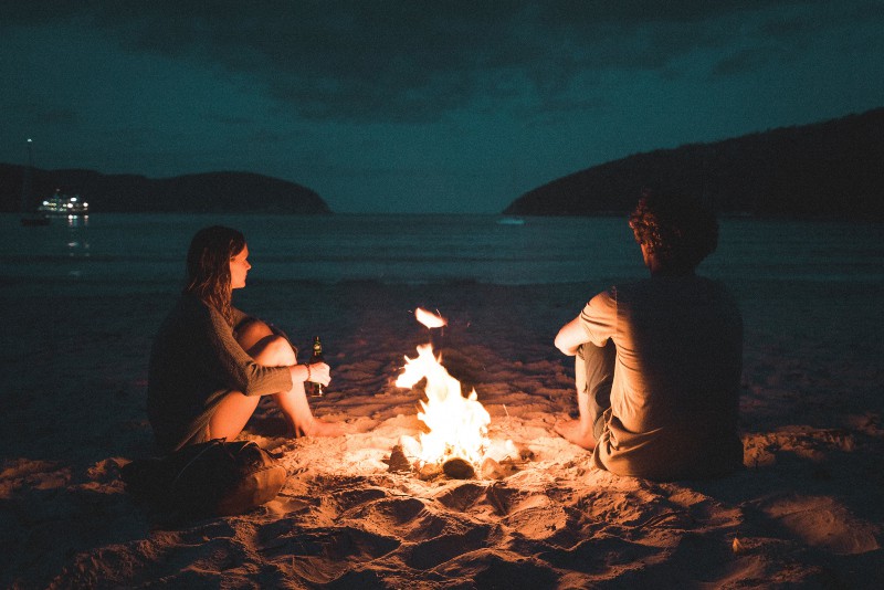 Mann und Frau mit Lagerfeuer sitzen am Meer