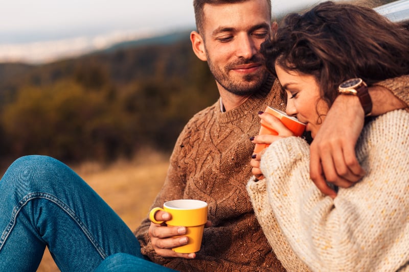 Paar im Sweatshirt trinkt Kaffee draußen