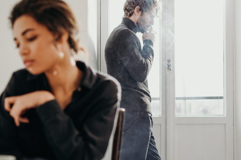 traurige Frau mit Mann, der im Hintergrund raucht