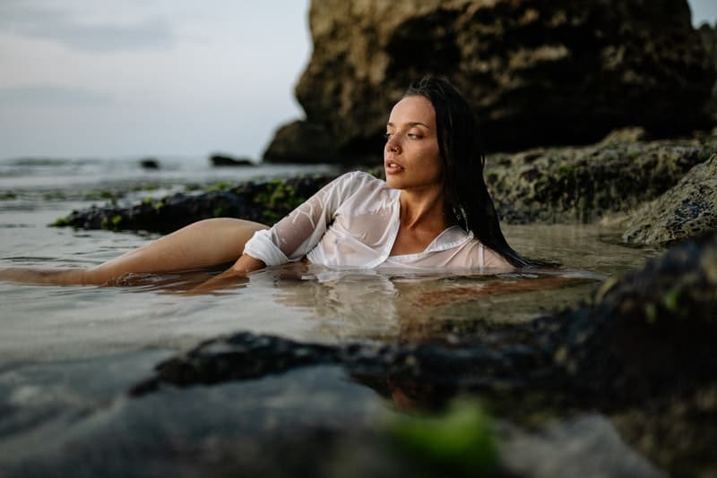 eine sexy Frau in einem weißen Hemd, die im Flachwasser des Meeres liegt