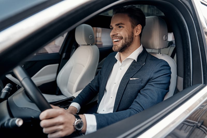lächelnder Mann im Anzug, der Auto fährt