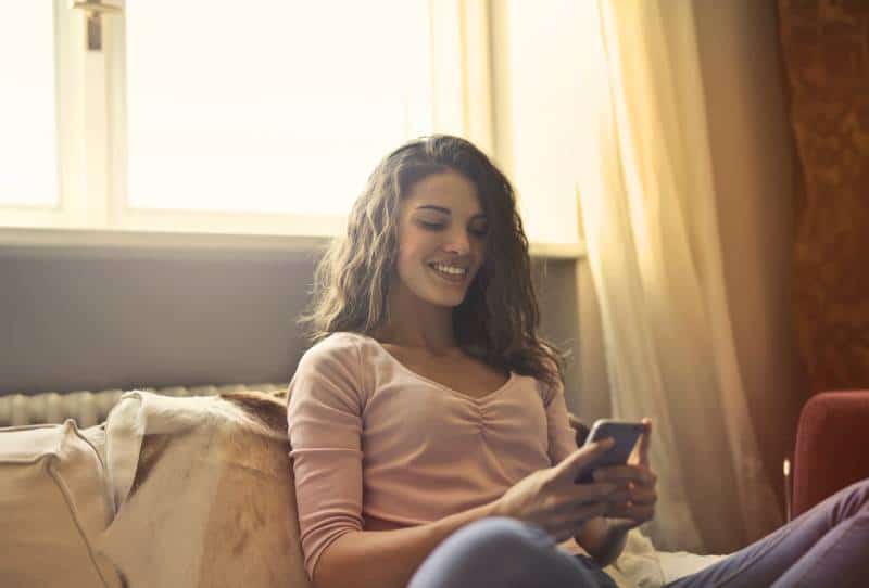 lächelndes Mädchen, das ihr Telefon zu Hause tippt