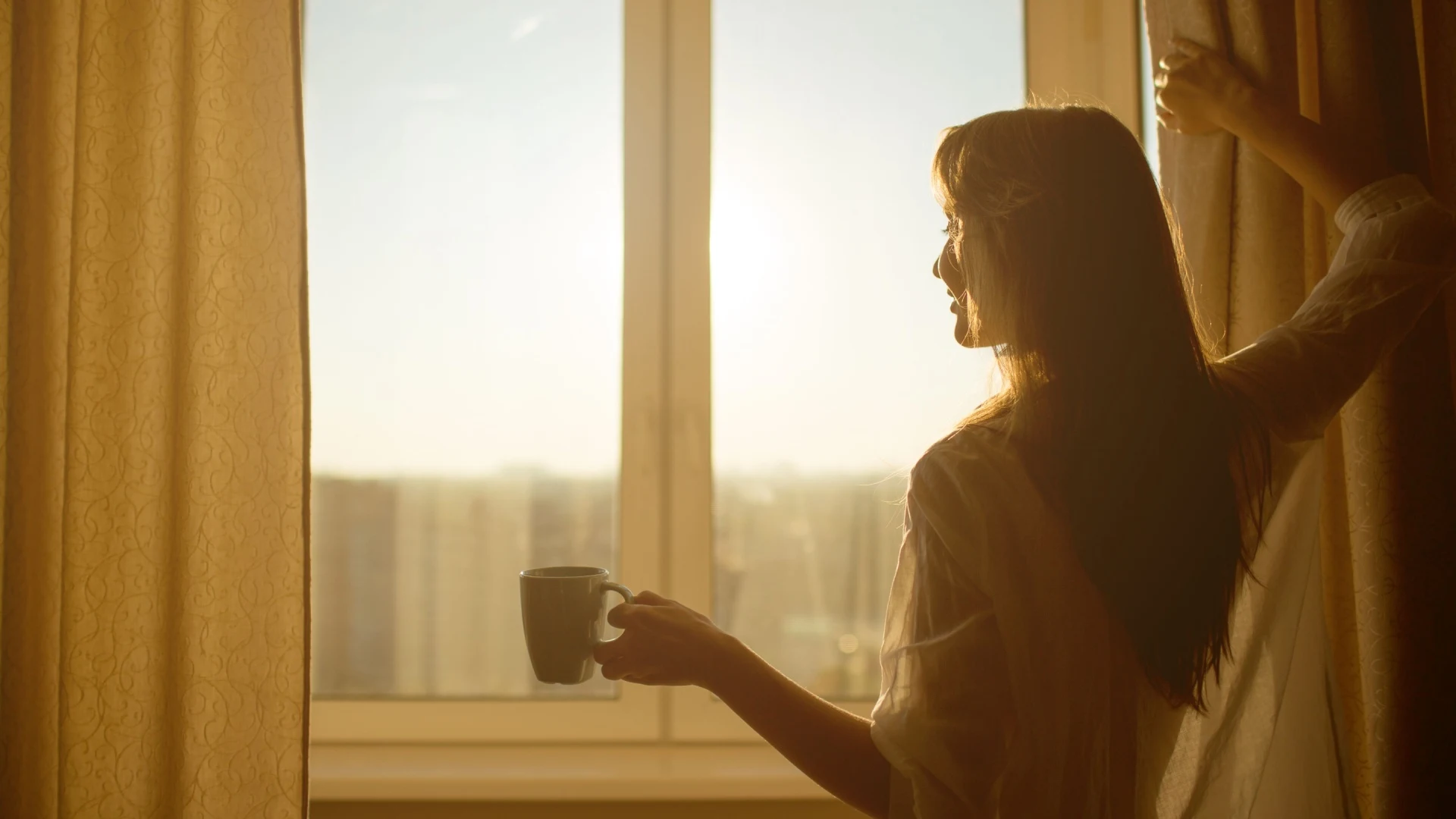 Frau steht vor Fenster mit Kaffee