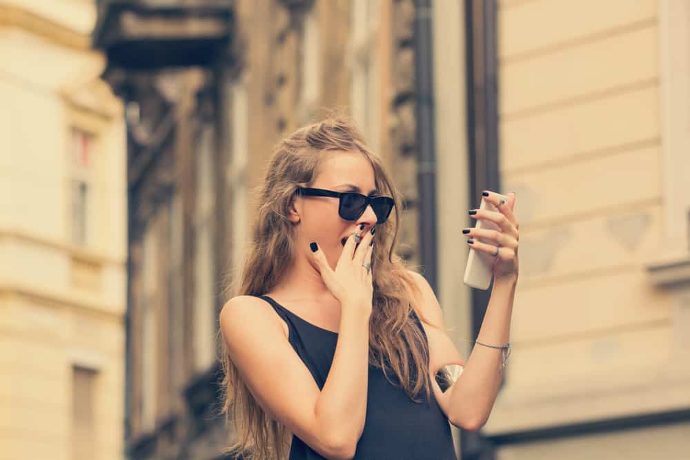 Die attraktive Blondine schaut überrascht auf ihr Handy