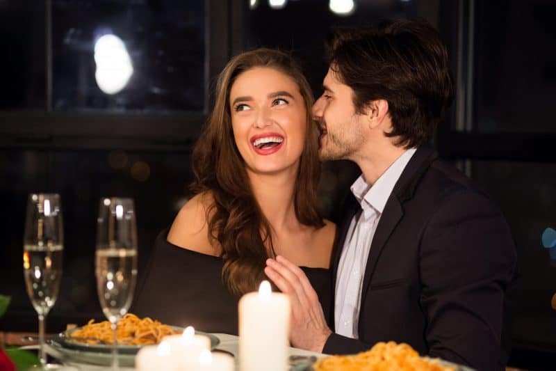 Ein Mann beim Abendessen im Restaurant flüstert einer lächelnden Frau etwas ins Ohr