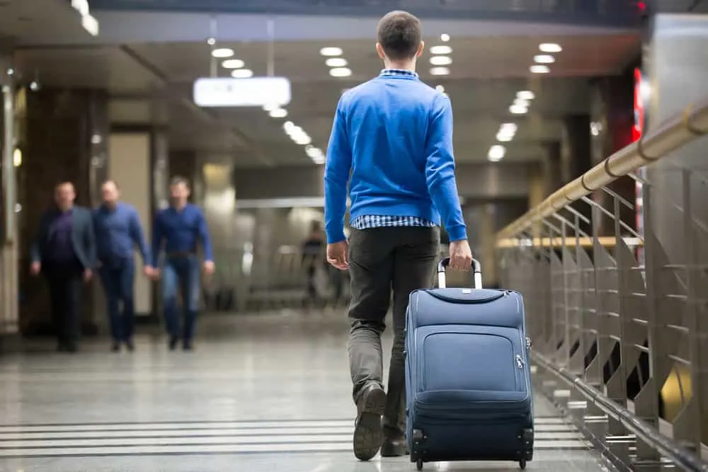 Ein Mann in einem blauen Pullover zieht am Flughafen einen Koffer