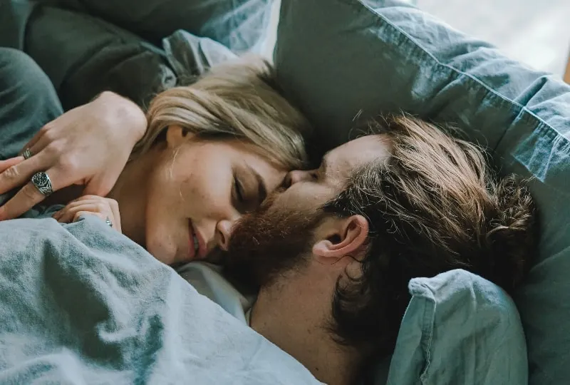Ein Mann küsst eine Frau auf die Stirn, während er im Bett liegt