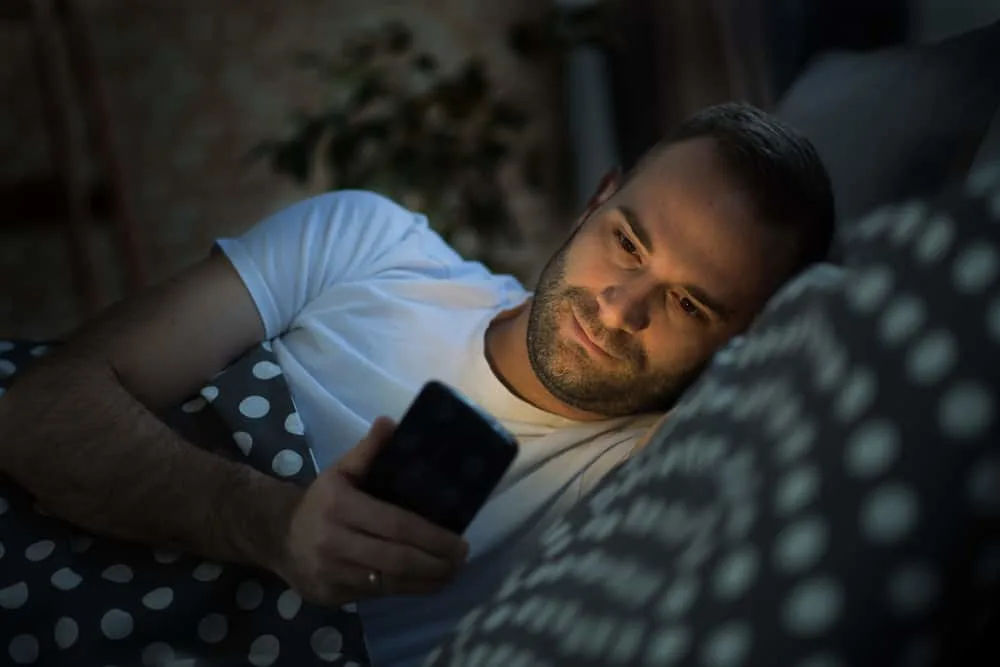 Ein Mann liegt auf dem Bett und schreibt eine Nachricht auf sein Handy