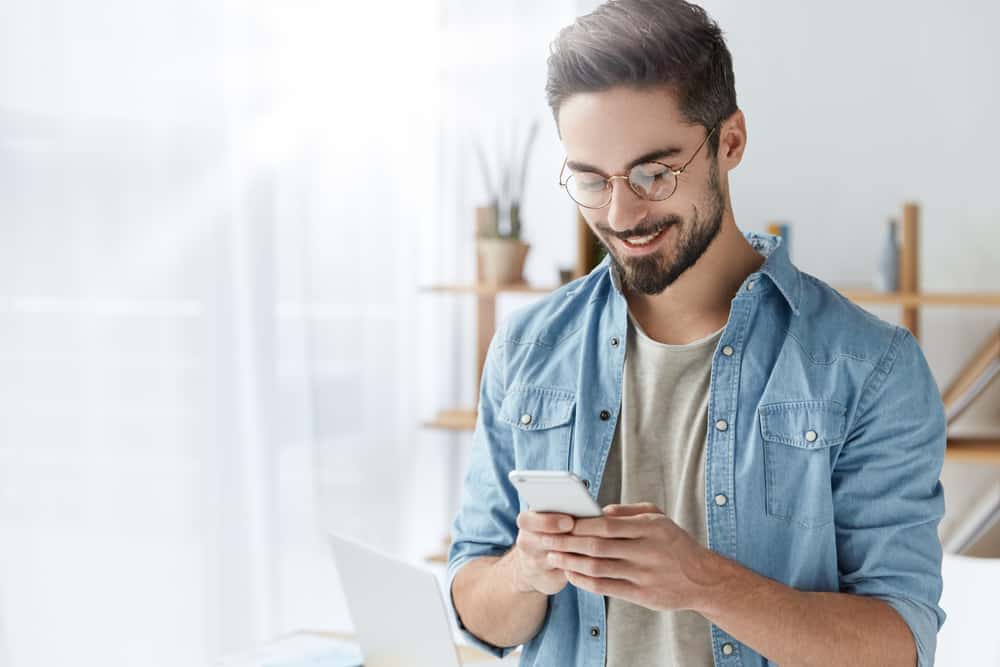 Ein lächelnder Mann in einem Jeanshemd schreibt eine SMS