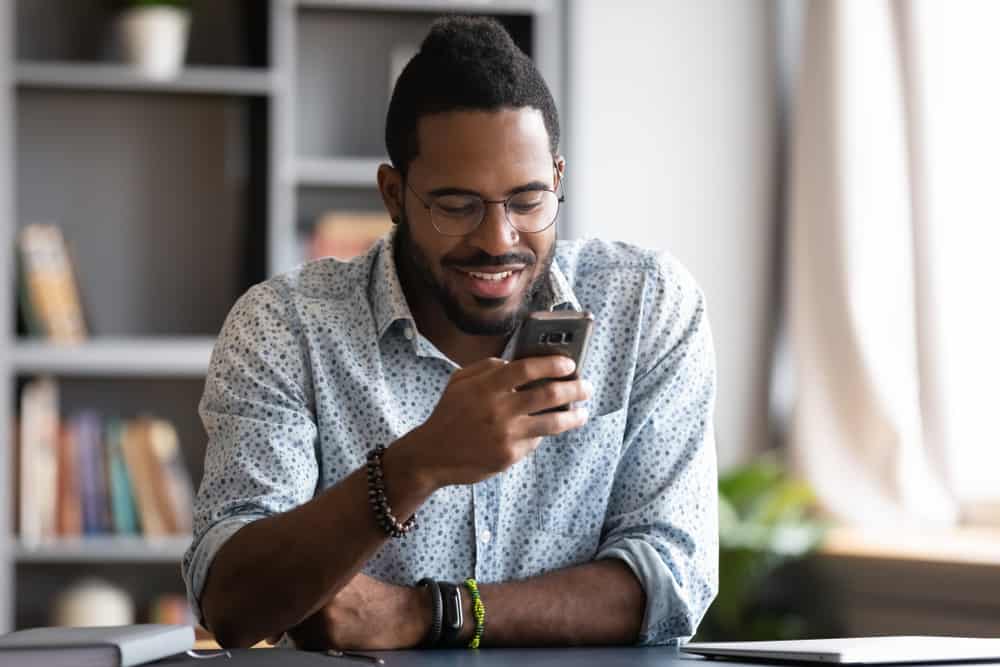 Ein lächelnder schwarzer Mann mit Brille schreibt eine SMS
