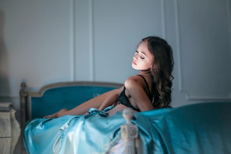 Eine hübsche Brünette in Dessous liegt allein auf einem Doppelbett